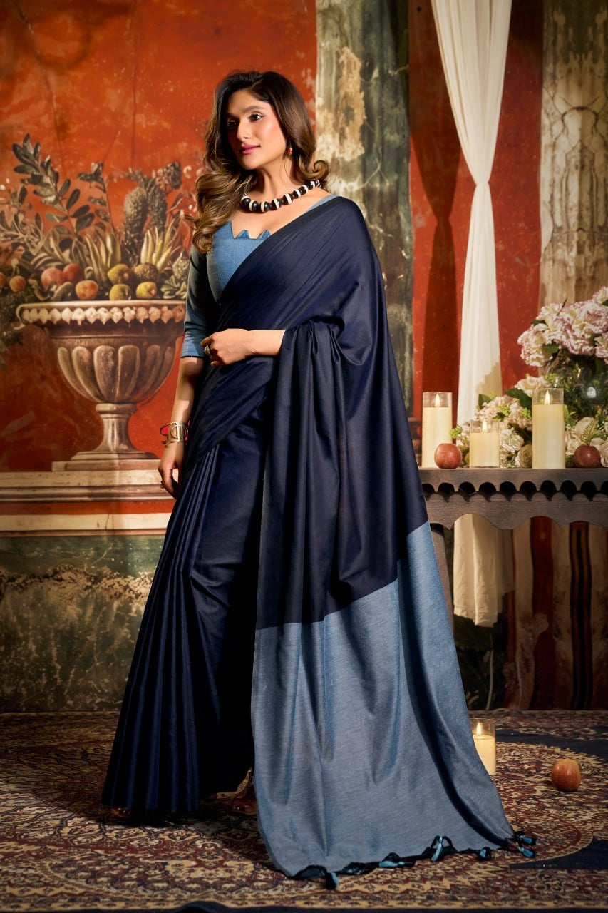 Woman in a blue saree standing in an elegant interior setting with decorative elements.